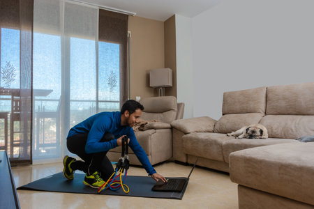 Latin man, doing a workout in his living room with a rubber band while taking an online classの写真素材