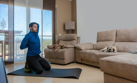 Latin man, doing a workout in his living room, does sit-ups, stretches and squatsの写真素材