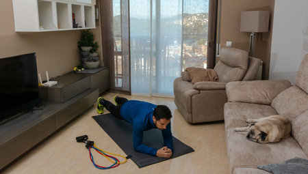 Latin man, doing a workout in his living room, does sit-ups, stretches and squatsの写真素材