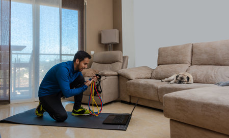 Latin man, doing a workout in his living room with a rubber band while taking an online classの写真素材