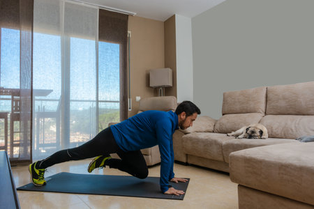Latin man, doing a workout in his living room, does sit-ups, stretches and squatsの写真素材