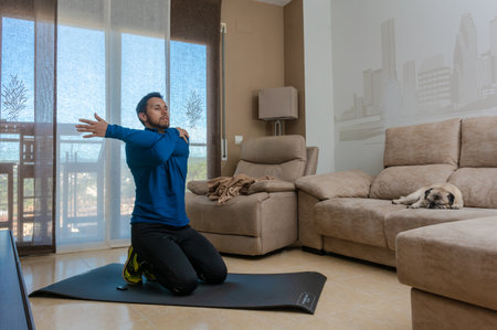 Latin man, doing a workout in his living room, does sit-ups, stretches and squatsの写真素材