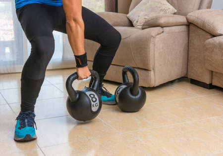 Latin man performing a cross fit workout at home with a pair of kettlebells.の写真素材