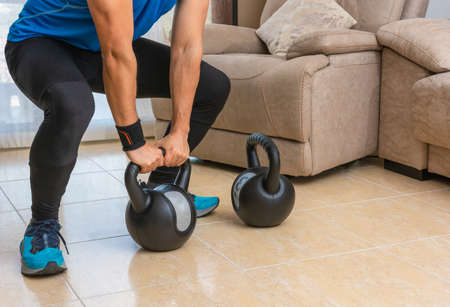 Latin man performing a cross fit workout at home with a pair of kettlebells.の写真素材