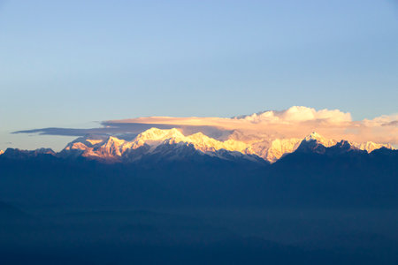 The snow-capped peaks glow with a golden hue, while the early morning light paints the sky in soft shades of pink and orange.の写真素材
