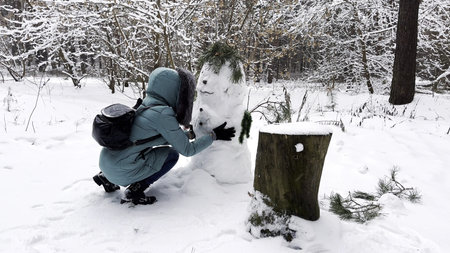 Happy woman building snowman at winter forest. Young girl having active leisure at snowy park....