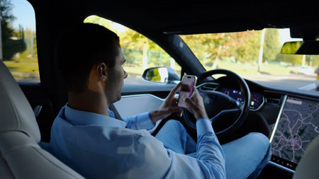 Successful businessman browsing modern smartphone while riding an autonomous self driving electric...