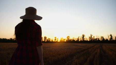 Female farmer going through the barley plantation at sunset. Young agronomist walking among wheat meadow at dusk. Beautiful scenic landscape. Concept of agricultural business. Close up Slow moの写真素材