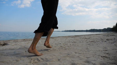 Bare feet of adult woman jogging on sand at the beach with seascape at background. Female legs...