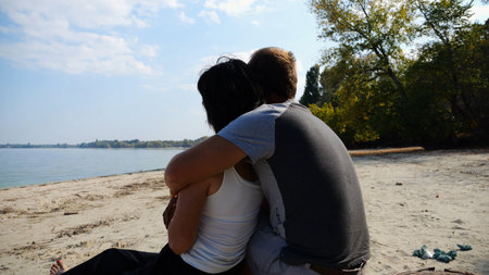 Romantic couple hugs during sitting on wooden log on the beach. Happy pair admiring a sea and...
