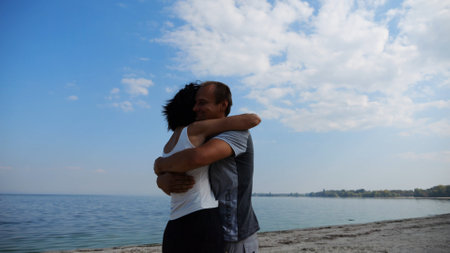 Couple holding hands of each other and walking at coast. Man taking woman in air and turning around at coastline. Happy pair having fun together on seashore at summer vacation. Concept of loveの写真素材
