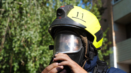 Young fireman connecting oxygen tank to the mask outdoor. Male fireguard in full equipment ready to...