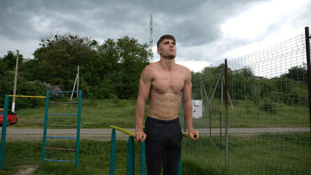 Young sportsman doing push ups on parallel bars at nature. Strong sporty man exercising at sports...