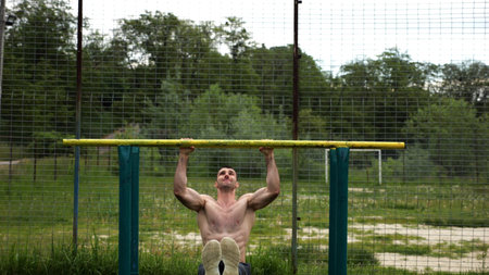 Hardy shirtless sportsman doing exercises on parallel bars at nature. Strong and muscular man...