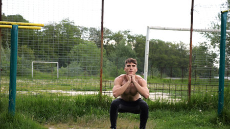 Male shirtless athlete doing squats at sports ground. Young sportsman working at summer nature. Strong sporty man exercising outdoor. Concept of active and sportive lifestyle. Slow motionの写真素材