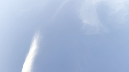White lines after flying airplane in blue sky at summer sunny day. Beautiful cloudscape at...