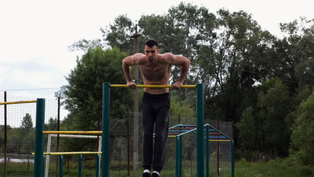 Hardy shirtless sportsman doing push ups on horizontal bar at nature. Strong and muscular guy...