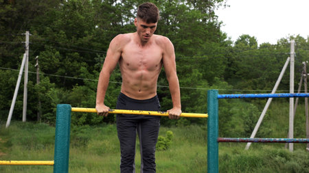 Hardy shirtless sportsman doing push ups on horizontal bar at nature. Strong and muscular guy...