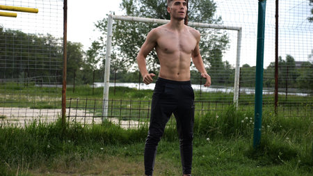 Male shirtless athlete doing squats at sports ground. Young sportsman working at summer nature. Strong sporty man exercising outdoor. Concept of active and sportive lifestyle. Slow motionの写真素材