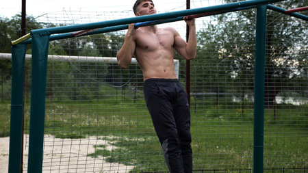 Young muscular sportsman doing pull ups at sports ground. Athletic guy exercising outdoor. Strong...