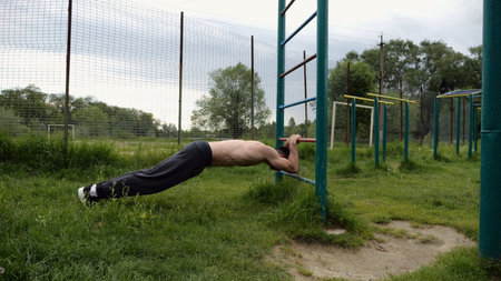 Young muscular athlete doing exercise on triceps at sport equipment outdoor. Male shirtless athlete...