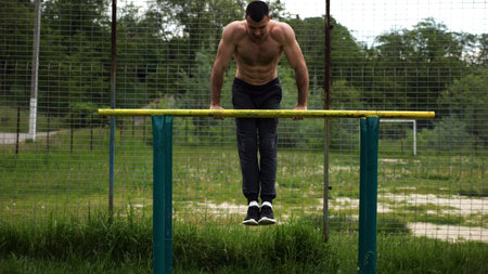 Hardy shirtless sportsman doing exercises on parallel bars at nature. Strong and muscular man...