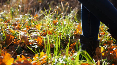 Low view to female feet in boots going along trail on fallen dry leaves. Legs of young woman...