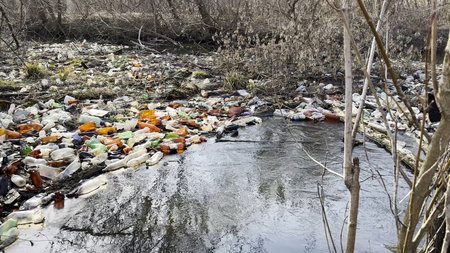 Dirty river is polluted with many plastic bottles. A lot of trash is dumped in open and freely available places at nature. Global environmental pollution problem. Concept of ecological disasterの写真素材