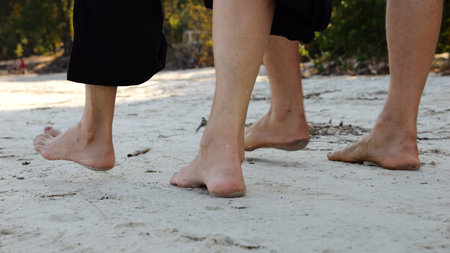 Male and female legs of pair walking on sandy beach. Bare feet of couple stepping along sand shore at sunny day. Lovers spending time together at resort. Concept of summer vacation or holidayの写真素材