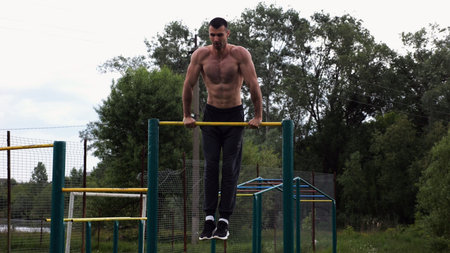 Hardy shirtless sportsman doing push ups on horizontal bar at nature. Strong and muscular guy...