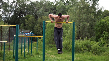 Hardy shirtless sportsman doing push ups on horizontal bar at nature. Strong and muscular guy...