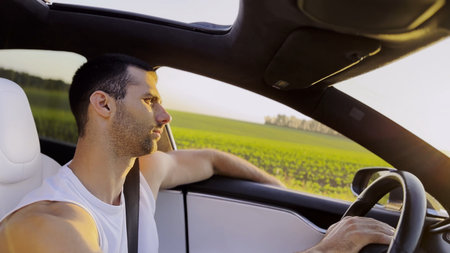 Profile of young handsome man driving a modern electric car with sunlight at background. Young male...
