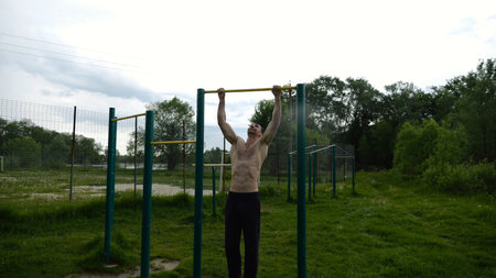 Muscular athlete doing pull ups on horizontal bar at sports ground. Young shirtless sportsman...
