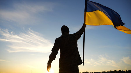 Silhouette of male military lifting blue-yellow banner in honor of the victory against russian...