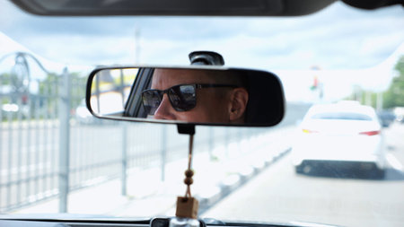 Eyes in sunglasses of male driver reflecting in rearview mirror while riding motor auto. Young guy...