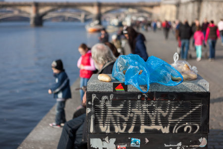 PRAGUE, CZECH REPUBLIC - MARCH 8th, 2014 - Litter bin on promenade of Vltava river with people in...