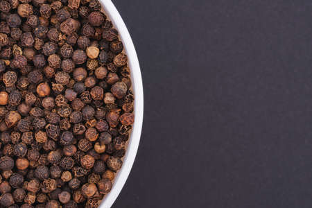 White glass bowl of black pepper. Isolated on a dark gray background. Top view close upの写真素材
