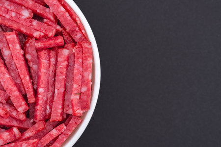 White glass bowl of sliced salami. Isolated on a dark gray background. Top view close upの写真素材