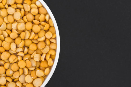 White glass bowl of yellow peas. Isolated on a dark gray background. Top view