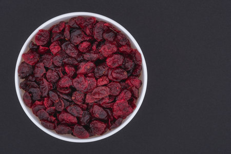 White glass bowl of dried cranberries. Isolated on a dark gray background. Top view close up photo