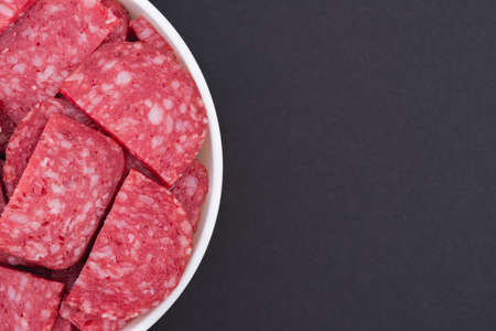 White glass bowl of sliced salami. Isolated on a dark gray background. Top view close upの写真素材