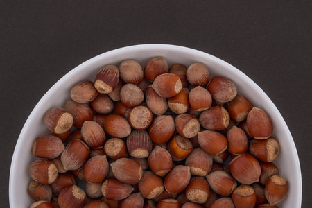 Hazelnuts in a white bowl. Top view isolated on brown background.