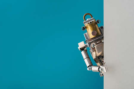 Portrait of a steampunk robot looking around the corner of a cyan and gray empty board with space for copyの写真素材