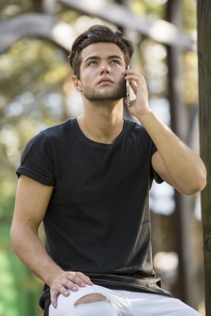 Handsome man doing a phone call, talking on cell phone, standing outdoor during daytime looking up.の写真素材