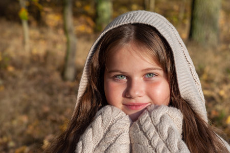 A young girl in a beige sweater with a hood. She smiles and looks at the cameraの写真素材