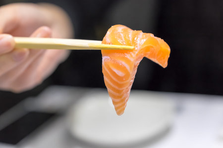 Hand holding Fresh salmon by chopsticks on blur women backgroundの写真素材