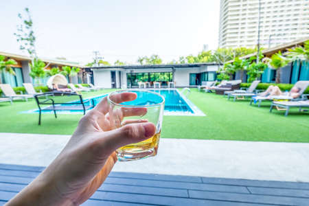 close-up of man hand holding glass with whisky ,swimming pool backgroundの写真素材