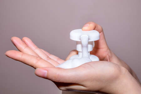 Female hands applying liquid soap close up on cream backgroudの写真素材