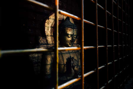 Old Buddha statue in the rusty iron cage.の写真素材