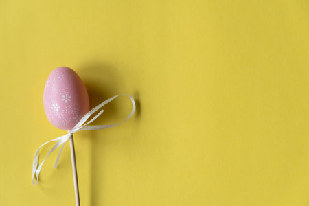 Easter pink egg on a wooden stick, beautiful yellow backgroundの写真素材